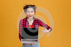 Joyful beautiful woman holding and pointing on blank screen laptop