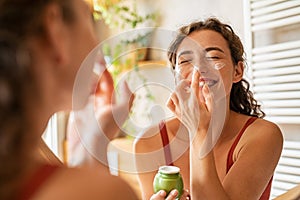 Joyful beauty woman applying cream on face