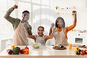 Joyful Black Family Shaking Fists Holding Hands Celebrating In Kitchen