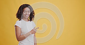 Joyful black girl pointing aside at copy space and smiling