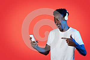 Joyful black guy listening to music online, using smartphone, headphones