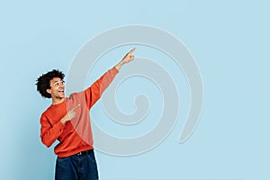 Joyful black guy pointing upwards on blue background