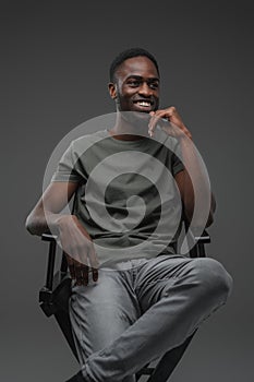 Joyful black guy sitting on chair against grey background