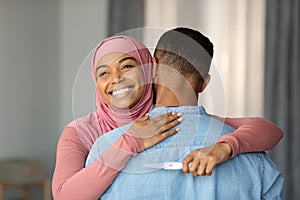 Joyful Black Islamic Lady Embracing Husband And Holding Positive Pregnancy Test