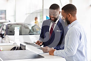 Joyful Black Man Buying Car, Signing Papers With Salesman In Dealership Office