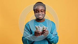 Joyful black man counting money, portrait in orange background in studio, guy with cash in hands