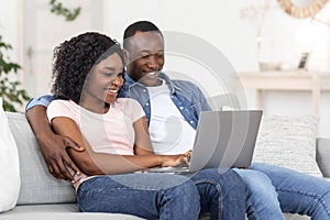 Joyful black man and woman watching photos on laptop