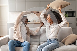 Joyful Black Millennial Couple Having Pillow Fight In Living Room