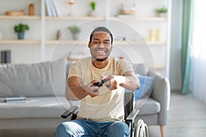Joyful black pareplegic man in wheelchair enjoying videogame on playstation at home