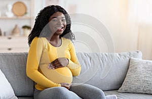 Joyful black pregnant woman hugging her big tummy