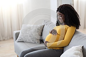 Joyful black pregnant woman hugging her big tummy, side view