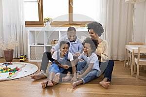 Joyful Black sibling kids and parents having fun on floor