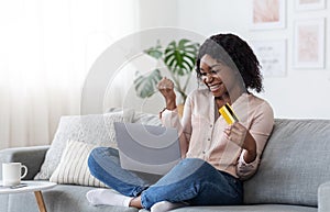 Joyful Black Woman Celebrating Successful Internet Shopping With Laptop And Credit Card