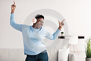 Joyful black woman listening to music in headphones and dancing