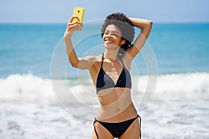 Joyful black woman taking selfie on smartphone near sea