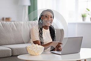 Joyful black woman watching movie on laptop at home