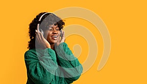 Joyful black woman in wireless headset listening to music