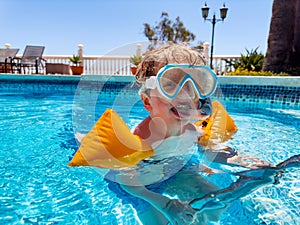 Joyful blonde boy with arm bands and a swimming mask in pool