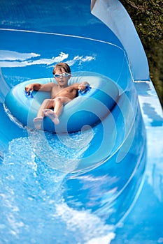 Joyful boy descends on an inflatable circle from the water slide in the water park, children's attractions in