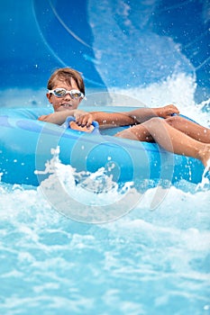Joyful boy descends on an inflatable circle from the water slide in the water park, children& x27;s attractions in
