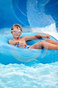 Joyful boy descends on an inflatable circle from the water slide in the water park, children& x27;s attractions in