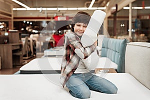 Joyful boy enjoying softness of orthopedic pillow rejoices in furniture store.