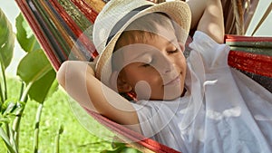 A joyful boy in hat relaxes in a garden hammock, capturing the essence of summertime, happy childhood, and vacation