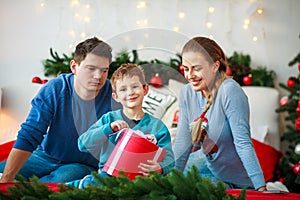 Joyful boy with parents opens a New Year`s gift box at Christmas home