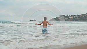 Joyful boy playing in sea surf. Happy teenager enjoying time at beach.