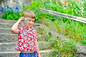 Joyful boy talking on the phone while standing in the park on the steps