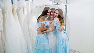 Joyful bride and bridesmaids hugging in wedding salon