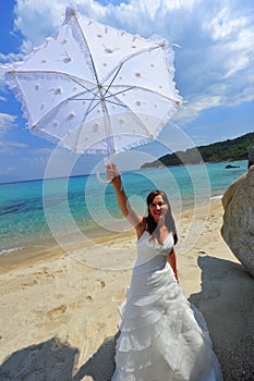 Joyful bride on exotic beach holding her umbrella