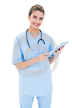 Joyful brown haired nurse in blue scrubs using a tablet pc