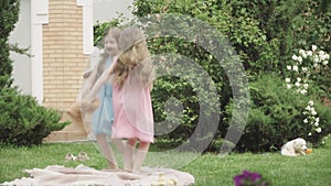 Joyful brunette twin sisters jumping with teddy bear on backyard. Wide shot portrait of cheerful Caucasian girls having