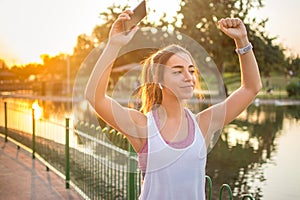 Joyful brunette woman wearing sportswear dancing while using smartphone and earpods outdoors