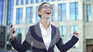 Joyful business woman making yes gesture holding smartphone, successful career