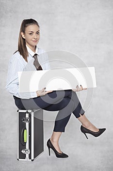 Joyful business woman sits on a suitcase and holds a commercial