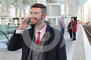 Joyful businessman calling by phone from train station