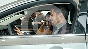 Joyful businessman with wife and son choosing car in showroom talking to sales manager