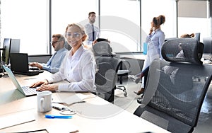 Joyful businesswoman in formalwear working on laptop in the modern office with collegues on the background