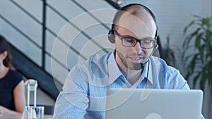 Joyful call centre agent with his headset talking looking at laptop