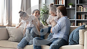 Joyful carefree parents playing with adorable little kids on sofa.