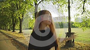 Joyful carefree teenage girl dancing in headphones in sunny summer park. Portrait of smiling cheerful Caucasian teenager