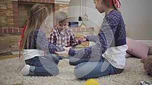 Joyful Caucasian girl teaching younger brother and sister playing a game. Happy teenager spending free time with kids at