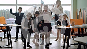 Joyful Caucasian schoolchildren and teacher throwing Covid face masks on the floor and stomping. Group of positive boys