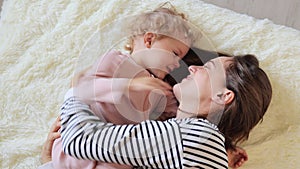 Joyful cheerful young brown haired woman with her little baby kid in home interior family lying on bed before sleeping and having