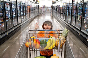 Joyful child boy in supermarket buys vegetables. Healthy food for children. Funny shopping. Cute kid with smile. A boy