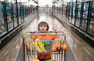 Joyful child boy in supermarket buys vegetables. Healthy food for children. Funny shopping. Cute kid with smile. A boy