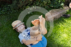 joyful child lies on the lawn, his bare feet tickled by a large ostrich feather