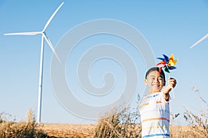 Boy's playful fascination near wind turbines holding a pinwheel toy